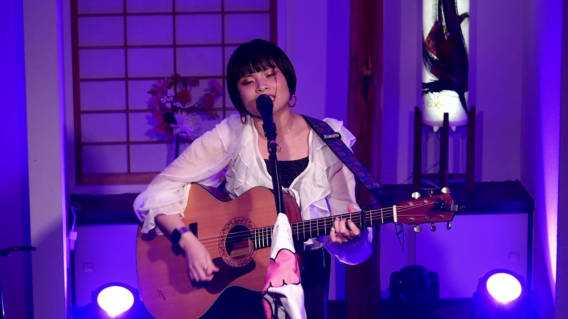 小川桃果(白いフリルのブラウスでアコースティックギターを弾きながら歌う)