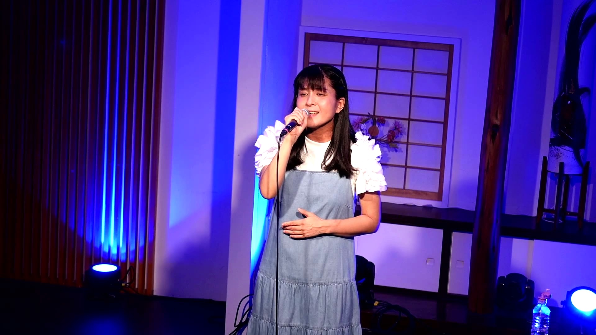 佐京こはな(青い照明の中でハンドマイクで歌う)