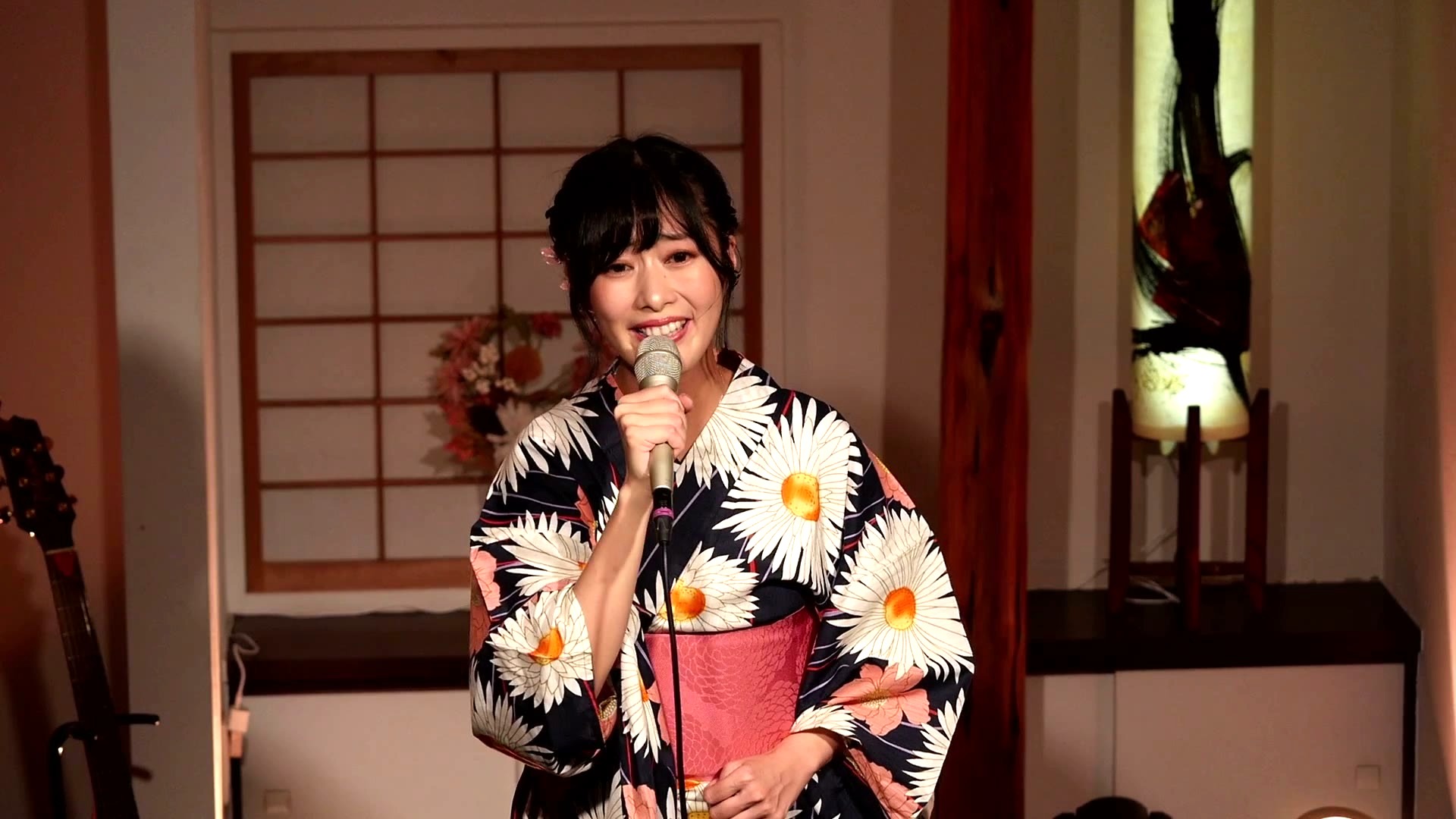 前田有加里(紺地に白い大輪の花柄の浴衣でハンドマイクを手に笑顔で歌う)